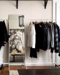 Clothing racks with assorted garments, a mirror, and a shelf with books and decor in a stylish room.