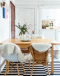 A dining room table on checkerboard flooring with sheepskin rugs on the chairs.