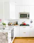 Modern kitchen with white cabinets, marble countertops, stainless steel appliances, and a red kettle on the stove.