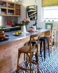 Wooden kitchen island with bar stools, geometric floor tiles, hanging lights, and a vase of flowers.