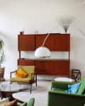 Mid-century modern living room with green armchairs, wooden sideboard, glass coffee table, and large arc floor lamp.