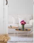 White living room with a white sofa, wicker coffee table, pink and purple flowers, and small potted plant.