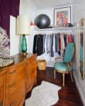Vintage-style closet with wooden dresser, green chair, clothes rack, framed poster, and exercise ball.