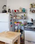 A stainless steel tiered storage rack wedged between a fridge and a stove to hold pantry items