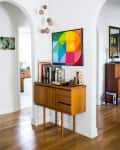 Mid-century modern console with books and decor, under a colorful geometric artwork, in a bright hallway.