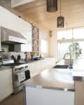 Modern kitchen with stainless steel countertops, floral curtain, pendant lights, and large window with a scenic view.