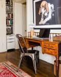 Home office with wooden desk, metal chair, laptop, desk lamp, and large dog portrait on the wall.