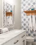 Bathroom with marble countertop, ornate mirror, wooden shelf with hooks, and blue patterned wallpaper.