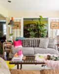 Eclectic living room with gray sofa, patterned pillows, plants, books, and colorful decor accents.