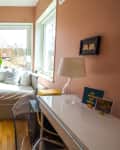 Cozy bedroom with pink walls, daybed with canopy, desk, clear chair, and table lamp by a window.
