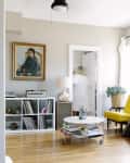 Living room with yellow chairs, white shelves, a round coffee table, and a portrait painting on the wall.