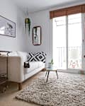 Living room with white sofa, black and white pillow, potted plants, wall art, and a TV on a white shelf unit.