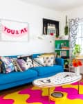 Colorful living room with a blue sofa, patterned pillows, vibrant rug, and a "You & Me" wall art.