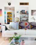 Eclectic living room with a white sofa, colorful pillows, plants, and art-filled walls.