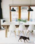 Dining room with wooden table, white chairs, pendant lights, and a small dog on a rug.