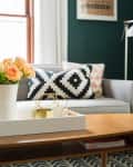 Living room with a gray sofa, geometric pillows, wooden coffee table, and vase of peach roses.