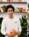 Person holding a terracotta pot in a plant shop, surrounded by shelves of various potted plants and greenery.