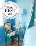 Bright blue bedroom featuring a bed with a fluffy white pillow, a green striped chair, and a glass lamp.