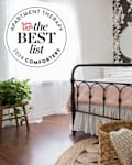 Cozy bedroom featuring a black metal bed frame, pink bedding, floral wallpaper, and a woven basket with a blanket.