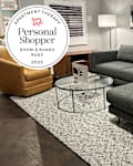 Rug displayed in living room setting at Room & Board store with Personal shopper seal to the left.