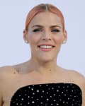 Person with short pink hair wearing a strapless black dress with silver embellishments, smiling.