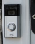 Silver video doorbell mounted on a stone wall next to a door handle.