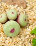 Green succulent plant resembling stones with purple markings, surrounded by pebbles and small green leaves.