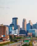 Minneapolis skyline with modern skyscrapers and busy highway in foreground at dusk.