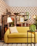 room with DIY wallpaper, gold loveseat, wood desk, shelves with l'objets, plants, gold rug