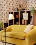room with DIY wallpaper, gold loveseat, wood desk, shelves with l'objets, plants, gold rug