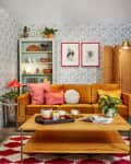 bright happy living space with gold velvet sofa, coffee table with yogi tea setup, patterned wallpaper, red and white rug, shelves with l'objets, plants
