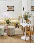 Head on view of a living room with white walls, a low couch with printed yellow and white ruffled cushions, two patchwork stools, and a small bistro table and chairs in the front right.