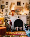 Cozy living room with mustard armchairs, colorful cushions, eclectic wall art, and a white fireplace adorned with decor.