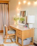 Dorm room with a wooden desk, mirror, string lights, and a bed with pink pillows.