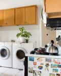 Kitchen with wooden cabinets, a dishwasher, stove with kettle, and a laundry area with washer, dryer, and potted plant.