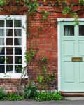 Mint green door on a red brick house with white-framed windows and climbing plants.