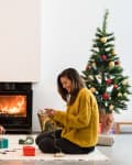 Two women wrapping gifts by a fireplace, with a decorated Christmas tree nearby.
