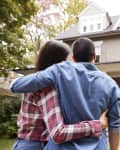 Couple embracing while looking at a two-story house with a porch.