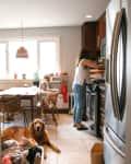 Woman cooking in a kitchen with a child at the table and a dog lying on the floor.