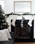 Christmas stockings hanging on a white fireplace mantel with greenery, next to a decorated tree and gray sofa.