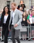 A smiling couple walks hand in hand, surrounded by a crowd taking photos.