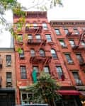 Historic brick apartment buildings with fire escapes and leafy trees in an urban setting.