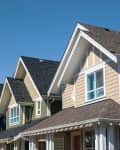 Row of suburban houses with gabled roofs and varied siding colors under a clear blue sky.