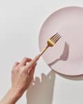 Hands holding a gold fork and knife over an empty pink plate.