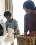 Woman and child doing laundry together, loading clothes into a front-loading washing machine.