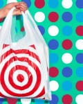 Hand holding a white plastic bag with red bullseye logo against a colorful polka dot background.