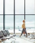 Person walking through an airport terminal with large windows and empty seating.