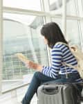 Woman in striped shirt sitting by airport window with suitcase, reading a map.