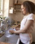 Woman washing dishes at a kitchen sink with plants on the windowsill.