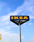 IKEA sign on a tall pole against a blue sky with flags below.